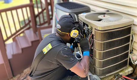 HVAC technician performing maintenance on an outdoor air conditioning unit to ensure efficient cooling at a residential property.