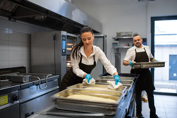 Restaurant staff preparing food in a commercial kitchen with industrial ovens and cooking equipment, representing the need for reliable commercial appliance repair services.