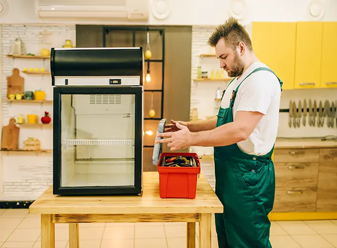 Technician performing maintenance on a commercial refrigeration unit in a kitchen setup.