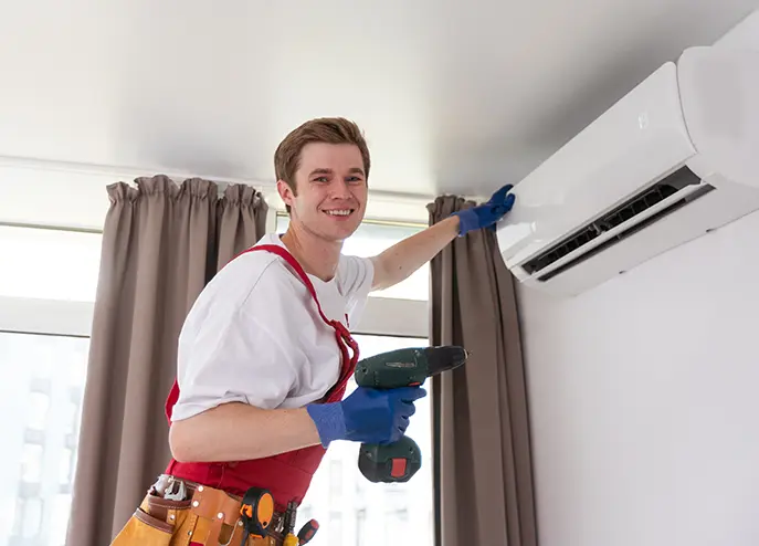 Smiling HVAC technician installing a wall-mounted air conditioning unit in a residential home.