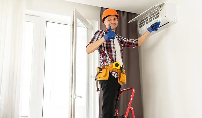 HVAC technician giving a thumbs-up during the installation of a wall-mounted air conditioning unit in a residential home.