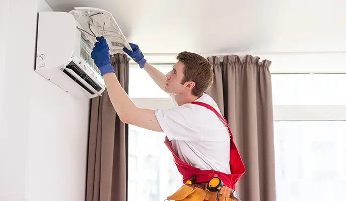 HVAC technician performing maintenance on a wall-mounted air conditioning unit in a residential home.