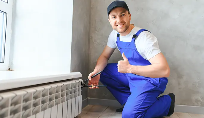 Smiling HVAC technician giving a thumbs-up while repairing a residential radiator for efficient heating.